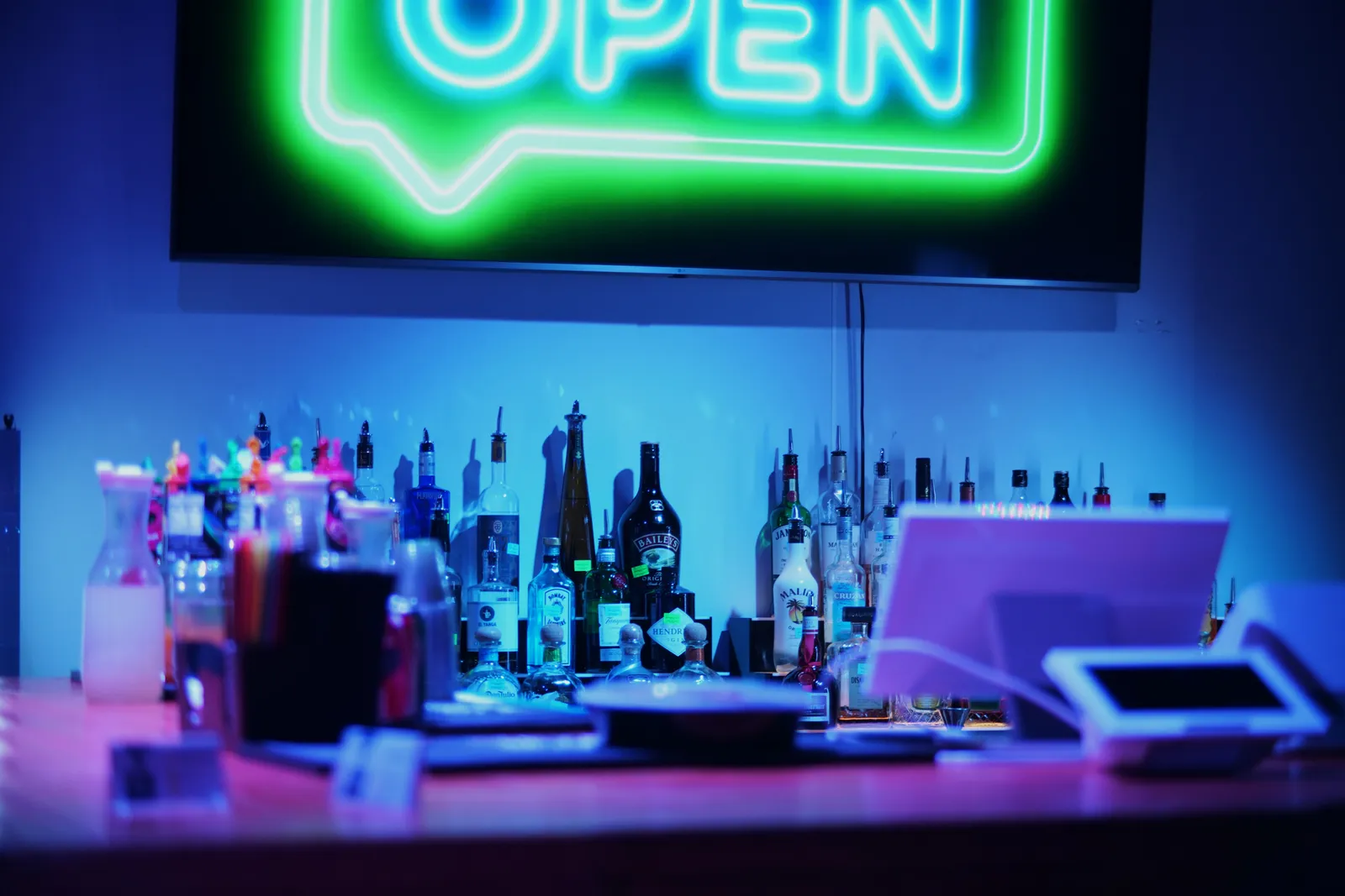 The fully stocked bar at Elegance at Event Masterz in South End Charlotte, lit in blue beneath a green neon open sign and set up for licensed bartenders to serve under the venue's full ABC license.